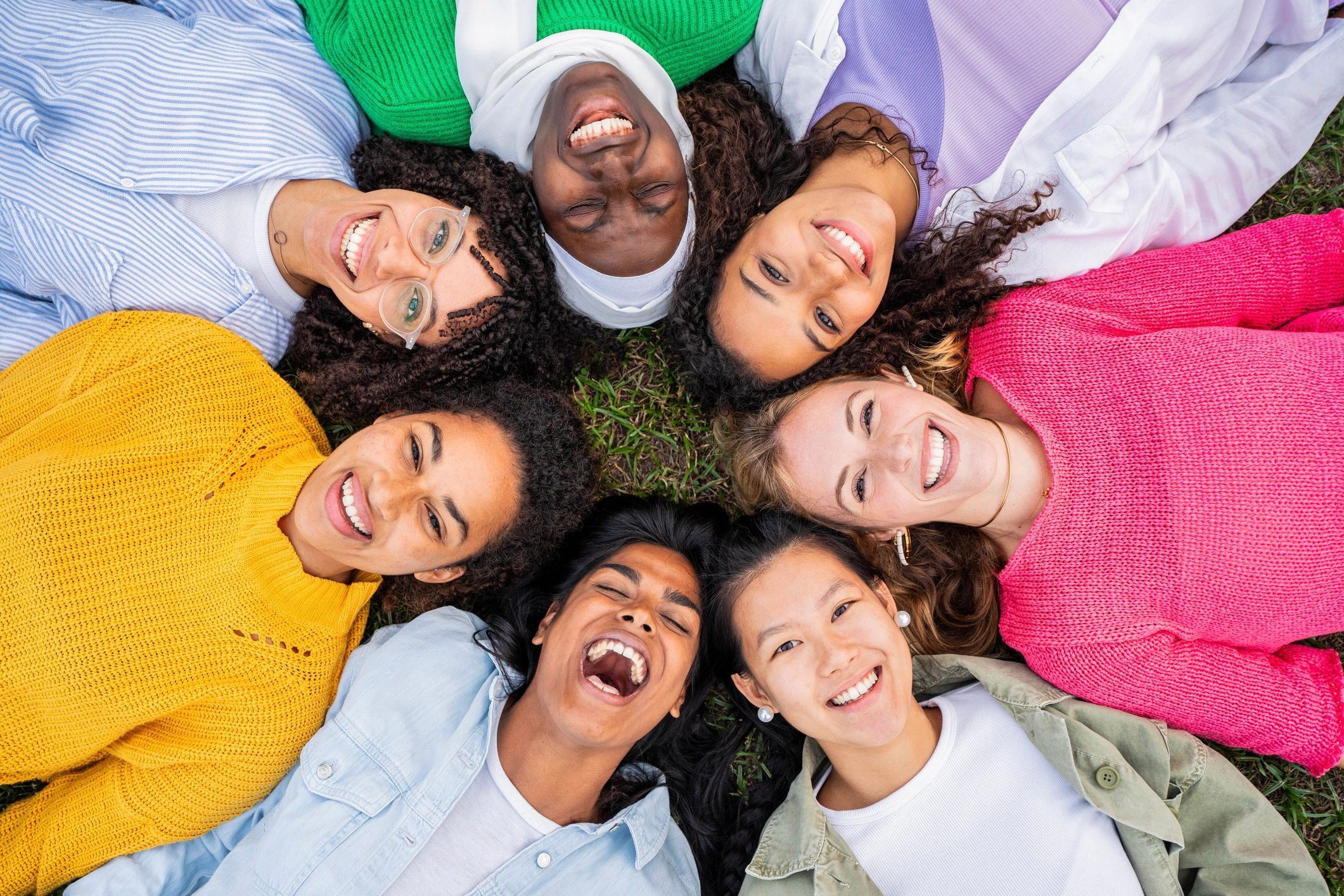 Diverse young people lying in a circle on grass